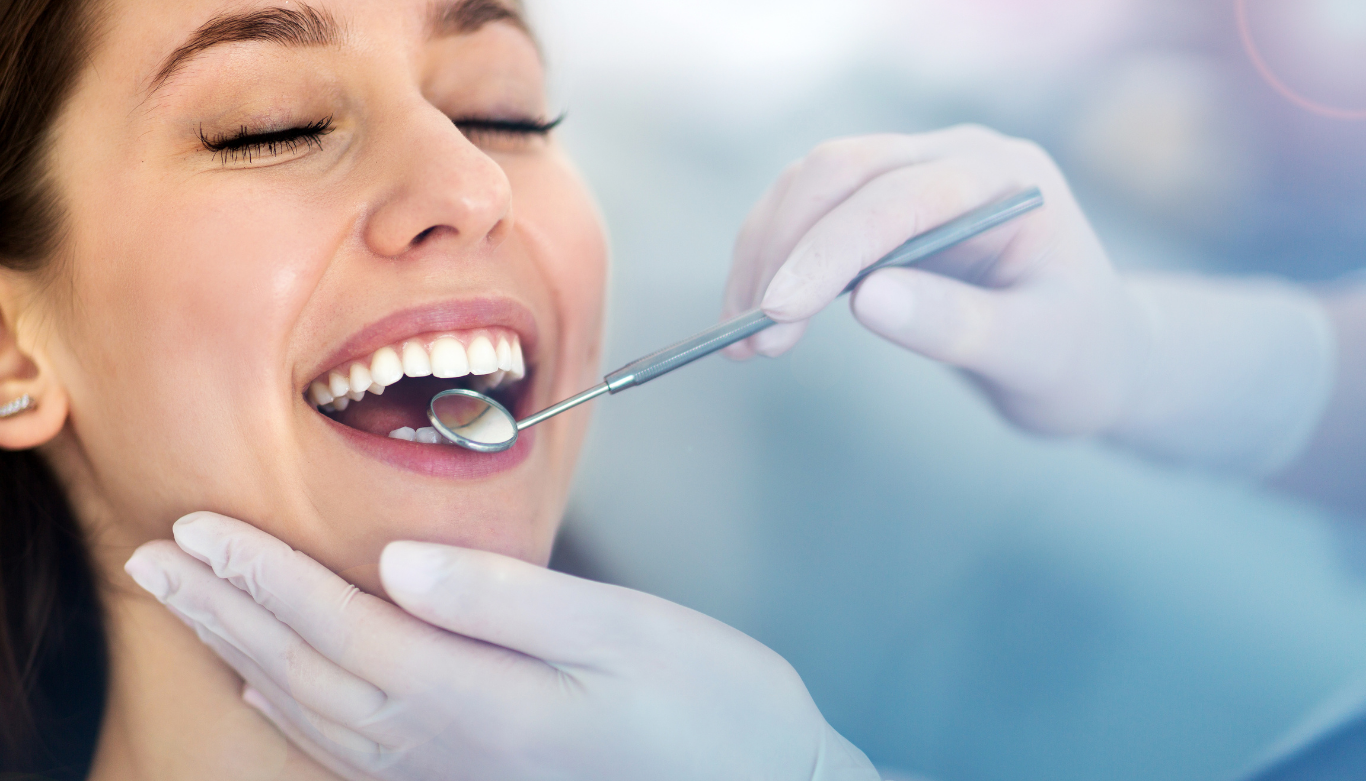 Female patient smiles during a dental checkup while a gloved clinician uses dental instruments in her mouth