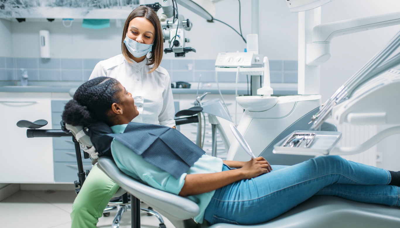 Patient reclining in a dental chair during a checkup with a masked clinician nearby in a modern clinic.